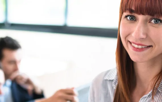 Young employee smiling with colleagues working behind